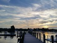 view from land looking down the dock with sunrise sky of soft shades of blue, orange and yellow and fluffy clouds