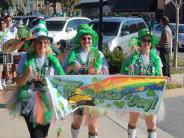 Three women dressed head-to-toe in St. Patrick's Day clothes cary a banner that says, "Happy St. Patrick's Day".