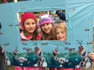 Three little girls hold up and squeeze their heads into a home-made, frozen-themed, picture frame.