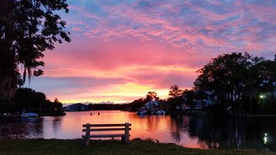 sunset over the water, taken from the park with a purple, pink and yellow sky and bench in the foreground 