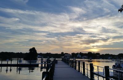 view from land looking down the dock with sunrise sky of soft shades of blue, orange and yellow and fluffy clouds
