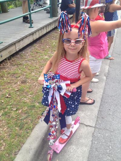 A girl proudly dressed head-to-toe in various American flag patterns, poses on her scooter for a 4th of July photo.