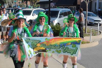 Three women dressed head-to-toe in St. Patrick's Day clothes cary a banner that says, "Happy St. Patrick's Day".