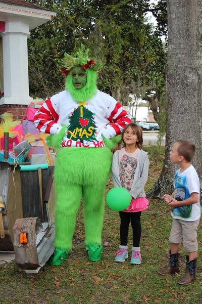 A candid photo of the Grinch as he stands with his hands on his hips, as a boy and a girl look approach for a photo op.